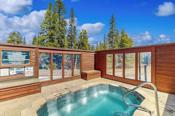 Ein Whirlpool mit Holzterrasse, umgeben von Glasscheiben, und ein Schild, das eine Poolkapazität von 8 Personen angibt.