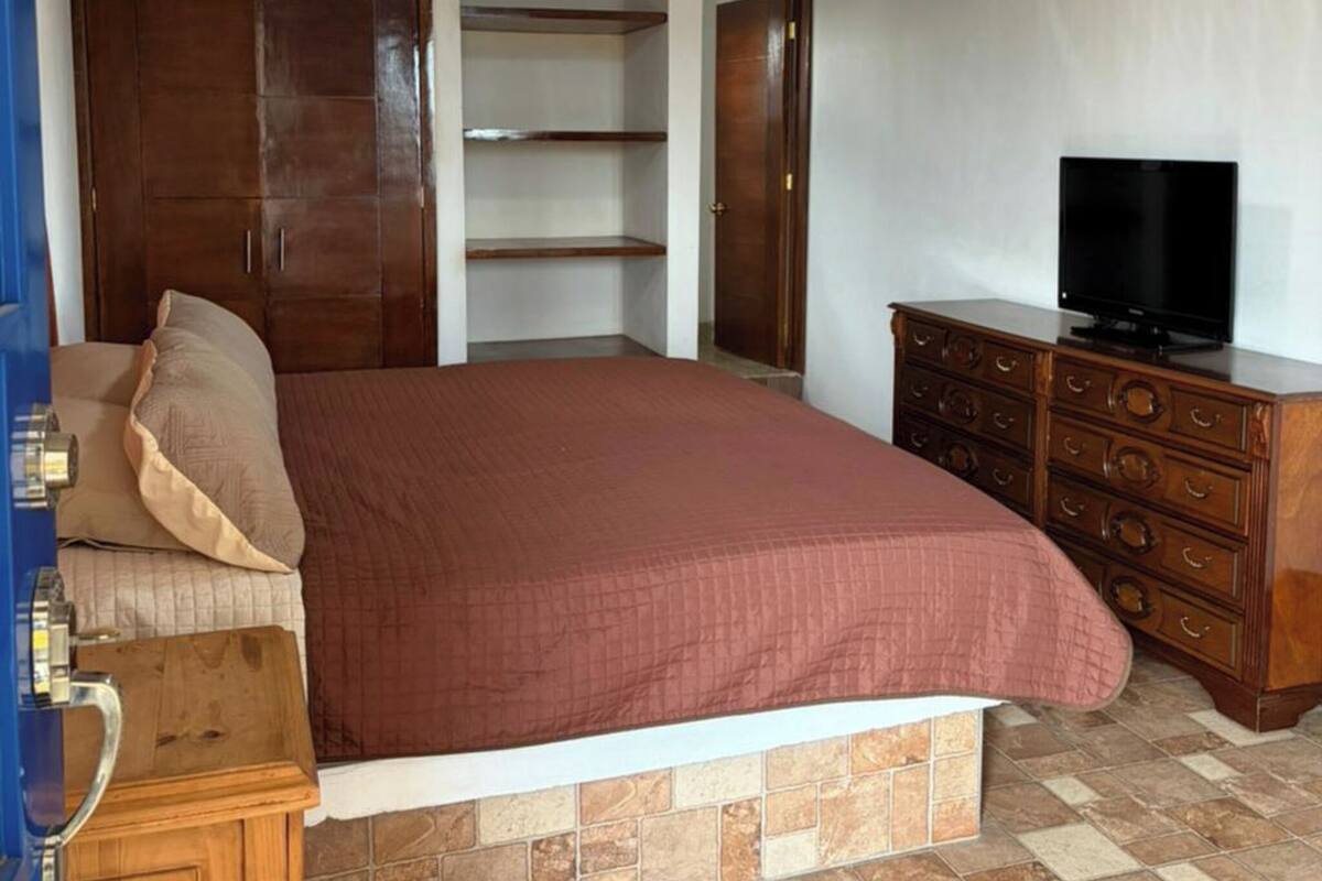 Un dormitorio con cama, televisor, armario y un pequeño aparador.