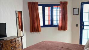 Un dormitorio con cama, cómoda, ventana con cortinas y puerta.
