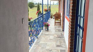 Un balcón cubierto con piso de baldosas, baranda de metal azul y una silla de madera.