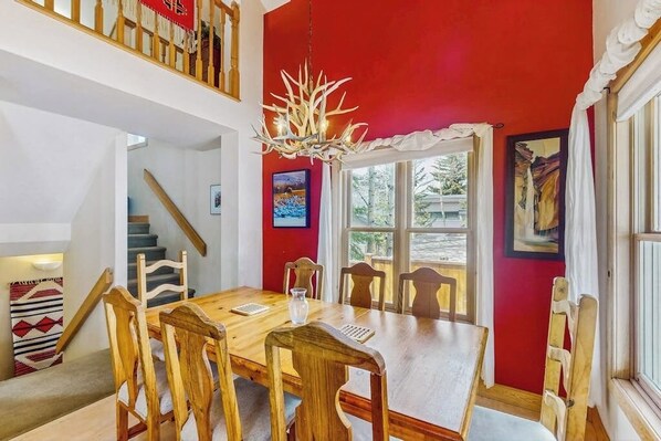 A dining area with a wooden table and chairs, a chandelier, and a red wall. - Victorian home with private hot tub, two blocks to Main Street (Breckenridge)