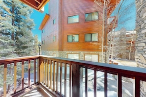 A multi-story building with a wooden facade, a stone base, and a balcony with a wooden railing. - Ski-in/out ground-floor condo with hot tubs, fireplace, gym & views (Breckenridge)