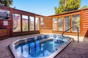 A hot tub with a wooden deck and glass walls, surrounded by a wooden cabin structure. - Ski-in/out ground-floor condo with hot tubs, fireplace, gym & views (Breckenridge)