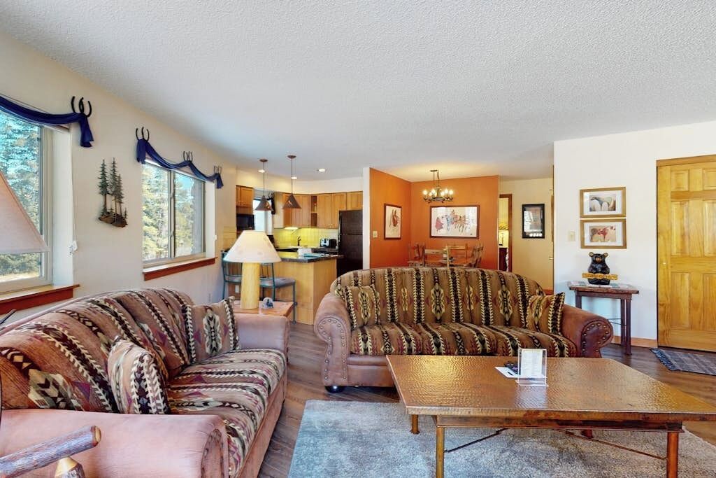 A living room with two patterned sofas, a coffee table, and a dining area with a chandelier.