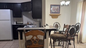 Una cocina con armarios oscuros, un refrigerador blanco, un comedor con sillas estampadas y una araña.