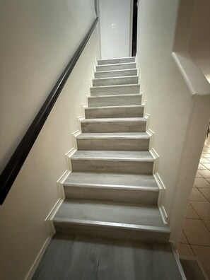 A staircase with white steps and a dark handrail, leading to a door with a light switch. - Welcoming 2-bedroom townhome with AC in Harlingen (Harlingen)