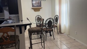 Un comedor con una cocina al fondo, una araña y un cuadro en la pared.