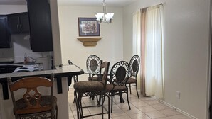 Un comedor con una barra de cocina, sillas, una lámpara de araña y un ventanal con cortinas.