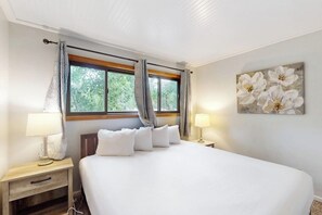 Ein Schlafzimmer mit einem Bett, zwei Nachttischen, einem Fenster mit Vorhängen und einem Wandbild mit Blumen.