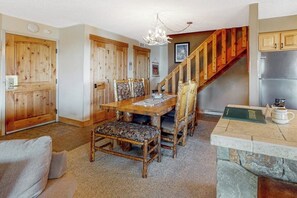A dining area with a wooden table and chairs, a chandelier, and a kitchen area with cabinets and a refrigerator. - Ski-in/out gold-rated condo with hot tubs, fireplace & gym (Breckenridge)