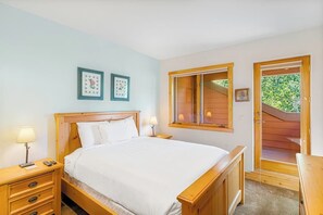 Ein Schlafzimmer mit einem hölzernen Bett, Nachttischen, einem Fenster und einer Tür zu einem Außenbereich.