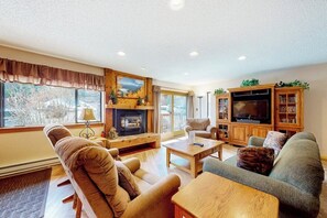 A cozy living room with a fireplace, a television, and a bookshelf. - Dreamy ski condo with balcony, hot tubs, fireplace, & gym (Breckenridge)
