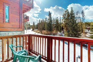 Eine Holzhütte mit Balkon, grünen Plastikstühlen und Blick auf einen verschneiten Wald.