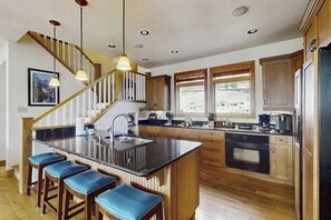 Eine Küche mit Kochinsel, Holzschränken, einem eingebauten Backofen und einer Treppe mit Geländer.