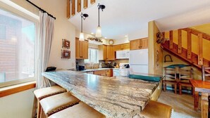 A kitchen with a large island, wooden stools, a staircase, and a view of the outside. - 2-story ski-in/out condo with fireplace, hot tubs, & gym (Breckenridge)