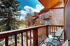 Ein hölzerner Balkon mit einem Metalltisch und Stühlen, der auf eine verschneite Landschaft und Gebäude blickt.