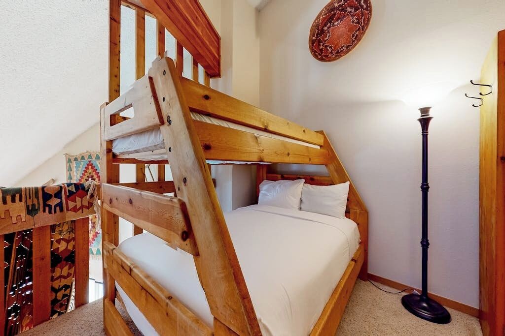 A bunk bed with a wooden headboard, a bedside lamp, and a patterned wall hanging.