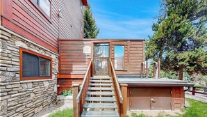 Una escalera de madera conduce a un espacio exterior cubierto con un muro de piedra y una ventana con persianas.