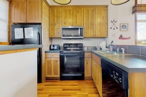 A compact kitchen with wooden cabinets, a black refrigerator, a microwave, a stove, and a dishwasher. - Ski-in/out condo with amazing views, washer/dryer, fireplace, & hot tub (Granby)