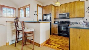 A kitchen with wooden cabinets, a microwave, a stove, and a bar area with chairs. - Ski-in/out condo with amazing views, washer/dryer, fireplace, & hot tub (Granby)