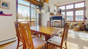 A dining area with a wooden table and chairs, a fireplace, and large windows with a view of the outdoors. - Ski-in/out condo with amazing views, washer/dryer, fireplace, & hot tub (Granby)