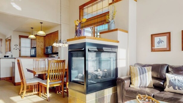 A modern kitchen with a central island, a dining area with wooden chairs, a fireplace, and a living room with a leather couch and a coffee table. - Ski-in/out condo with amazing views, washer/dryer, fireplace, & hot tub (Granby)