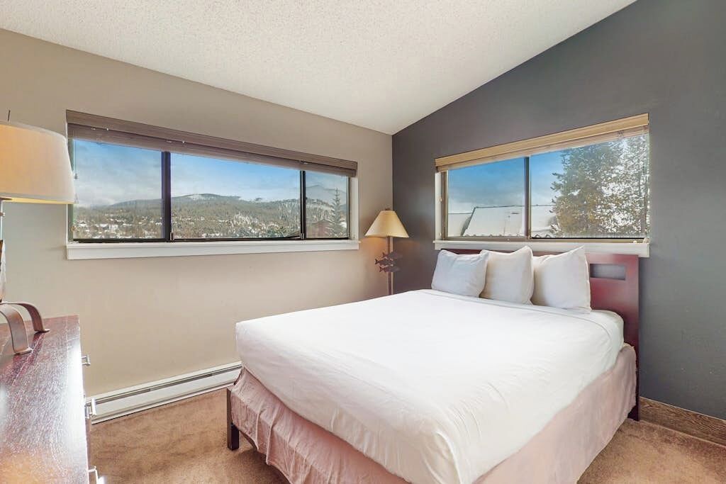A bedroom with a bed, two windows, a nightstand, and a lamp.