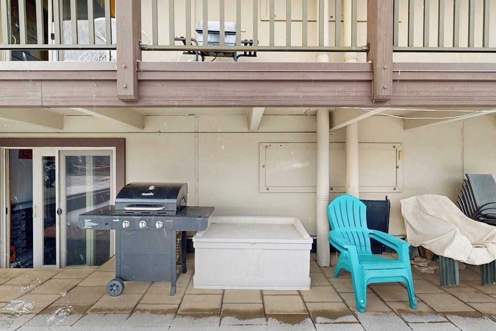 Een terras met een barbecue, een witte opbergkist en een turquoise stoel.