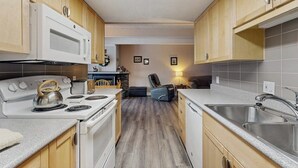 A compact kitchen with wooden cabinets, a microwave, stove, and a sink. - Shuttle to lifts from condo w/ panoramic views (Breckenridge)