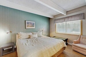 Quarto com cama, mesa de cabeceira, cadeira, janela com persianas e um quadro na parede.