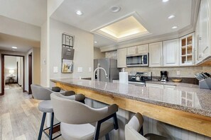A modern kitchen with a granite countertop, stainless steel appliances, and a bar area with stools. - Updated Breck Condo w/ Fireplace, Balcony Views & Walkable Location (Breckenridge)