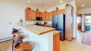 A kitchen with wooden cabinets, a granite countertop, a refrigerator, and bar stools. - Townhouse with a ski lodge feel with mountain view, W/D, fireplace & balcony (Keystone)