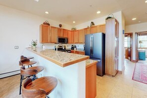 Eine Küche mit Holzschränken, einer Granit-Arbeitsplatte, einem Kühlschrank und Barhocker.