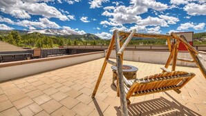 Eine Dachterrasse mit Schaukel, Feuerstelle und Blick auf schneebedeckte Berge.