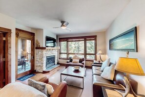Ein Wohnzimmer mit Kamin aus Stein, Deckenventilator, einer Couch, einem Couchtisch und einem an der Wand befestigten Fernseher.