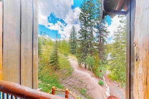Eine Holzterrasse mit Blick auf ein bewaldetes Gebiet und einen unbefestigten Weg.