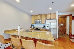 Eine Küche mit Granit Arbeitsplatten, Edelstahlgeräten, Holzschränken und einer Bar mit Barhocker.