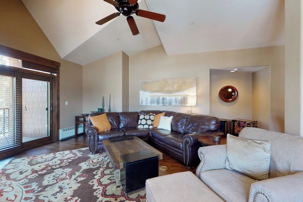 A living room with a sectional sofa, a coffee table, a ceiling fan, and a large window.