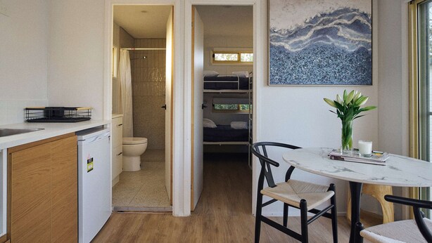 Une cuisine compacte équipée d’un lave-vaisselle, un coin repas avec une table et des chaises, une douche et un lit dans la pièce adjacente.