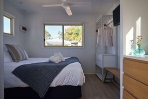 A bedroom with a bed, a window, a ceiling fan, a wardrobe, and a bench. - Clyde B 13 - Family Cabin Sleeps 6 with Bunks (Mollymook)