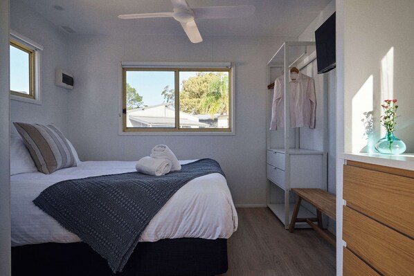 Ein Schlafzimmer mit Bett, Fenster, Deckenventilator, Kleiderschrank und einer Sitzbank.