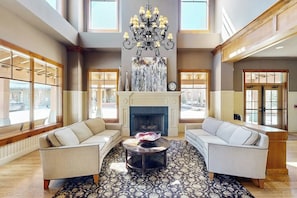 Eine geräumige Lobby mit Kamin, zwei Sofas, einer Kristallleuchtre und großen Fenstern.