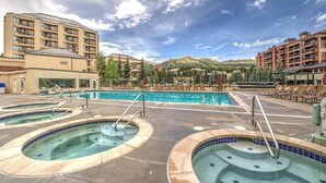 Ein Hotel mit Poolbereich, der Whirlpools und Liegestühle bietet, umgeben von Gebäuden und Bergen.