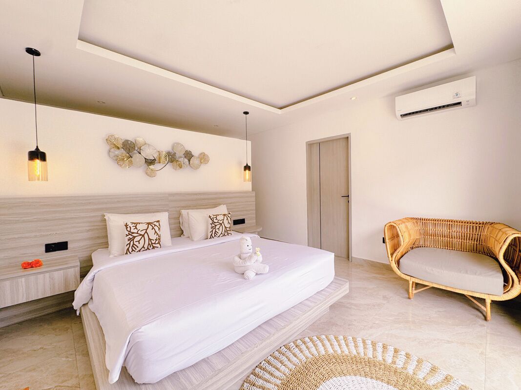 A modern bedroom with a large bed, bedside tables, a wicker sofa, and a wall-mounted air conditioner.