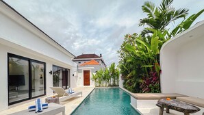 A swimming pool with lounge chairs and a stone bench, surrounded by lush greenery and a white building with large windows. - Canggu Luxury Villa – Private Pool (Badung)