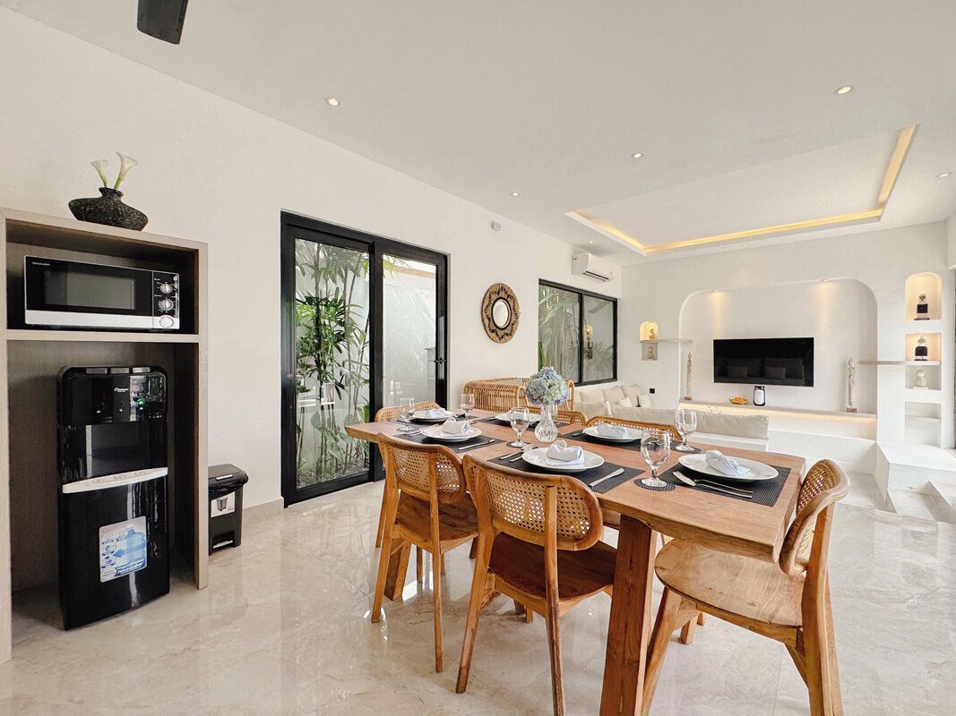 A modern dining area with a wooden table set for four, surrounded by wicker chairs.