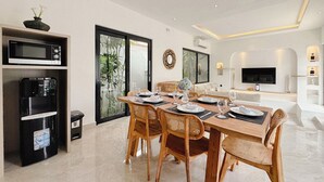 A modern dining area with a wooden table set for four, surrounded by wicker chairs. - Canggu Luxury Villa – Private Pool (Badung)