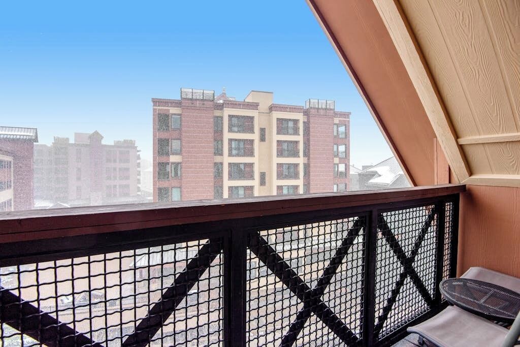 Un balcon doté d’une rambarde en treillis métallique, d’un espace salon avec des coussins et offrant une vue sur des immeubles à plusieurs étages.