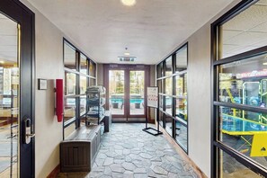 A hallway with a stone floor, large windows, and a view of an outdoor area with a pool. - Ski-in/out condo with outdoor pool, hot tub & gorgeous views of mountains/town (Breckenridge)