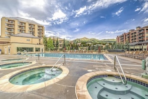 A hotel with multiple swimming pools, a mountainous backdrop, and a clear sky. - Walk-to-lift condo with gas fireplace, hot tubs, pool, gym & steam room (Breckenridge)